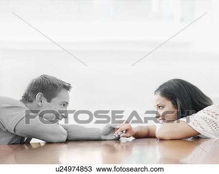 Stock Image - Affectionate young couple holding hands across table. Fotosearch
