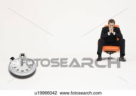 Stock Image - Anxious businessman sitting on chair with stopwatch showing time representing loss of time. Fotosearch