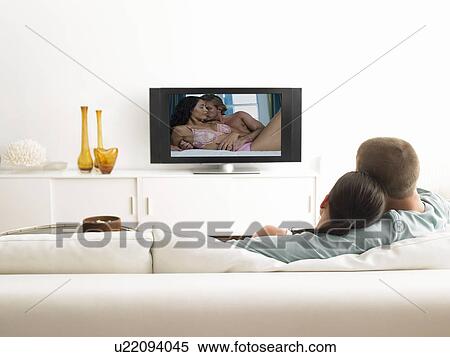 Stock Photography - Back view of affectionate couple on sofa watching television. Fotosearch