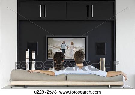 Stock Photo - Back view of couple watching movie on television in living room. Fotosearch