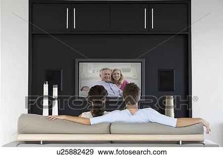 Stock Photo - Back view of couple watching movie on television in living room. Fotosearch