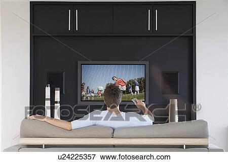 Back view of mid-adult man changing channels with television remote control in living room View Large Photo Image Stock Photo - Back view of mid-adult man changing channels with television remote control in living room. Fotosearch