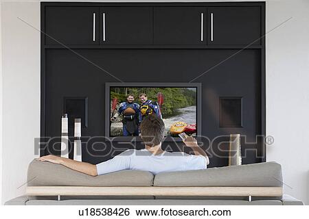 Back view of mid-adult man changing channels with television remote control in living room View Large Photo Image Stock Photograph - Back view of mid-adult man changing channels with television remote control in living room. Fotosearch