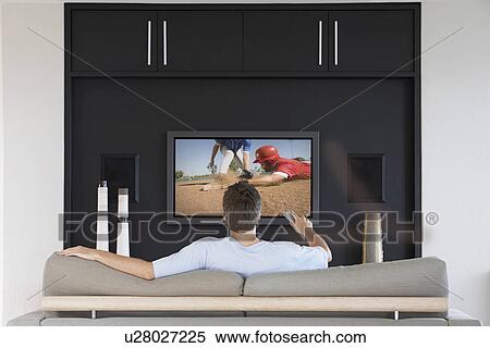 Stock Photography - Back view of mid-adult man changing channels with television remote control in living room. Fotosearch