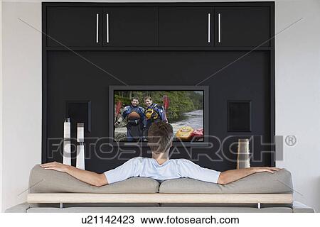 Back view of mid-adult man watching television in living room View Large Photo Image Stock Image - Back view of mid-adult man watching television in living room. Fotosearch
