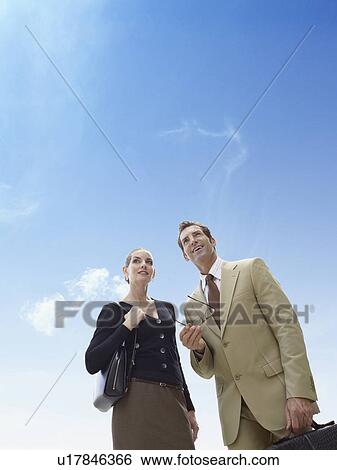Stock Photograph - Business man and woman standing against blue sky. Fotosearch
