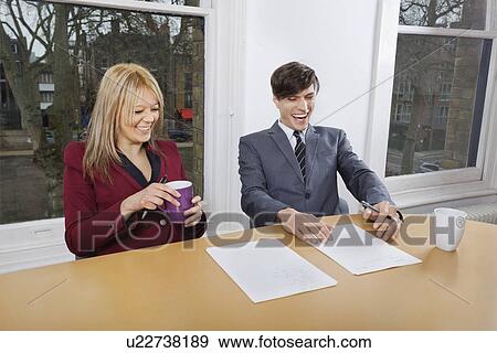 Cheerful young businesspeople with coffee mugs and documents at conference table View Large Photo Image Stock Photo - Cheerful young businesspeople with coffee mugs and documents at conference table. Fotosearch