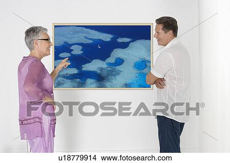 Couple discussing vacation plans against white wall with photograph View Large Photo Image Picture - Couple discussing vacation plans against white wall with photograph. Fotosearch