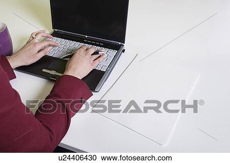 Stock Image - Cropped image of businesswoman's hands using laptop at desk. Fotosearch