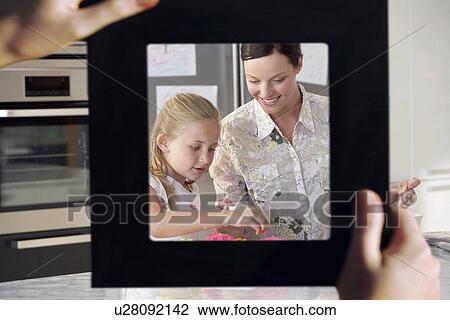 Stock Image - Female hand framing mother and daughter baking together in kitchen. Fotosearch