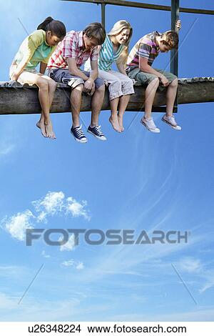 Four teenagers sitting on wooden bridge against blue sky View Large Photo Image Picture - Four teenagers sitting on wooden bridge against blue sky. Fotosearch