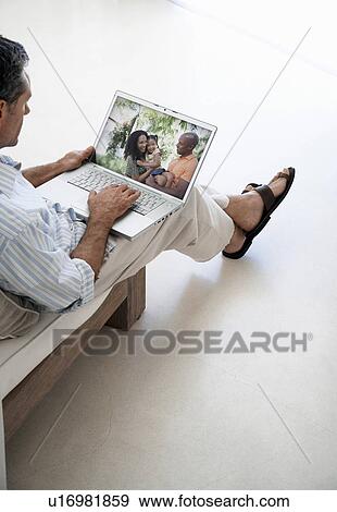 Middle-aged man browsing through family photographs on laptop at home View Large Photo Image Stock Photo - Middle-aged man browsing through family photographs on laptop at home. Fotosearch