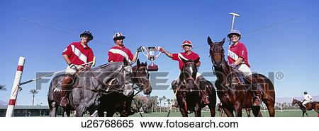 Stock Photography - Multiethnic polo team celebrating with trophy on field. Fotosearch