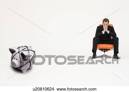 Pensive businessman on chair and piggybank tied with rope representing financial difficulties View Large Photo Image Picture - Pensive businessman on chair and piggybank tied with rope representing financial difficulties. Fotosearch