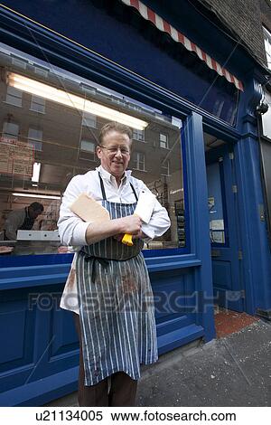 Stock Photography - Portrait of a happy senior butcher standing outside shop with cleaver. Fotosearch