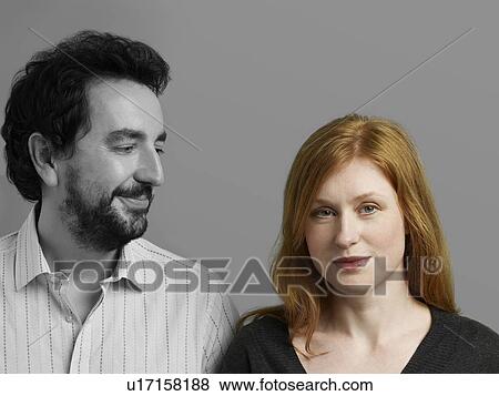 Stock Photo - Portrait of beautiful mid-adult woman with man looking at her against gray background. Fotosearch