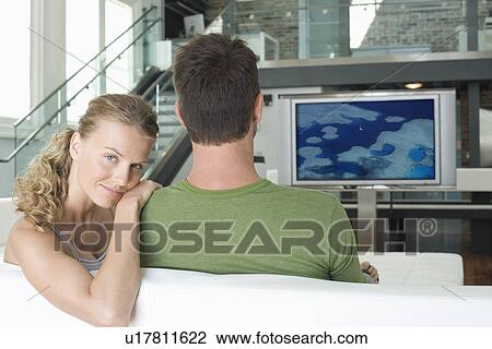 Portrait of young Caucasian woman with man watching television in living room View Large Photo Image Stock Image - Portrait of young Caucasian woman with man watching television in living room. Fotosearch