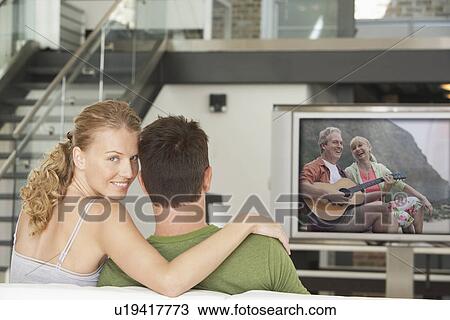 Portrait of young Caucasian woman with man watching movie on television in living room View Large Photo Image Stock Image - Portrait of young Caucasian woman with man watching movie on television in living room. Fotosearch
