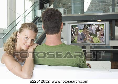 Portrait of young Caucasian woman with man watching movie on television in living room View Large Photo Image Stock Image - Portrait of young Caucasian woman with man watching movie on television in living room. Fotosearch
