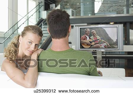 Portrait of young Caucasian woman with man watching movie on television in living room View Large Photo Image Stock Image - Portrait of young Caucasian woman with man watching movie on television in living room. Fotosearch