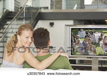 Portrait of young Caucasian woman with man watching movie on television in living room View Large Photo Image Stock Image - Portrait of young Caucasian woman with man watching movie on television in living room. Fotosearch