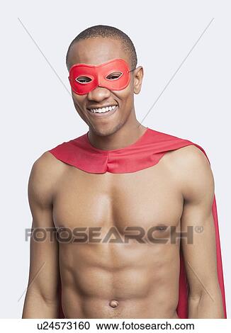 Stock Image - Portrait of young shirtless man in superhero costume smiling against gray background. Fotosearch