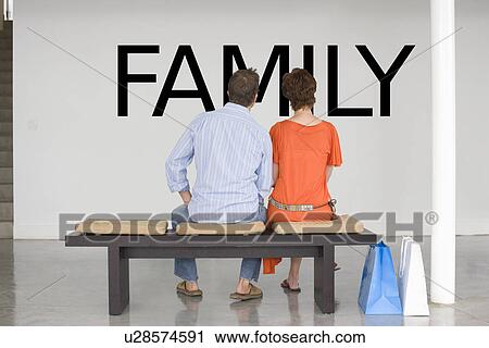 Rear view of couple seated on bench reading English text on wall View Large Photo Image Stock Image - Rear view of couple seated on bench reading English text on wall. Fotosearch