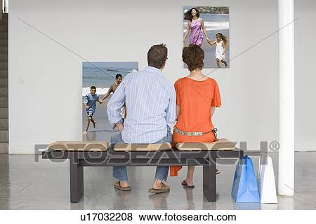 Rear view of couple seated on bench looking at photographs representing future planning View Large Photo Image Stock Photo - Rear view of couple seated on bench looking at photographs representing future planning. Fotosearch