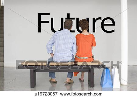 Stock Photo - Rear view of couple seated on bench reading English text on wall. Fotosearch