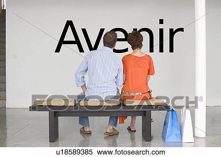 Rear view of couple seated on bench reading French text "Avenir" (future) on wall View Large Photo Image Stock Photography - Rear view of couple seated on bench reading French text "Avenir" (future) on wall. Fotosearch