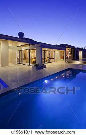 Stock Image - Rear view of luxury villa at night time with swimming pool. Fotosearch