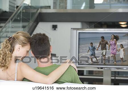 Stock Photograph - Rear view of young couple watching television in living room. Fotosearch