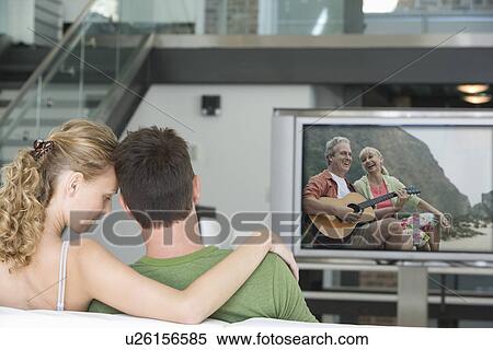 Rear view of young couple watching television in living room View Large Photo Image Stock Photography - Rear view of young couple watching television in living room. Fotosearch