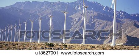 Stock Image - Row of power generating windmills in front of mountain range. Fotosearch
