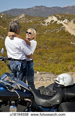 Stock Photo - Senior couple embrace next to motorcycle in the desert. Fotosearch