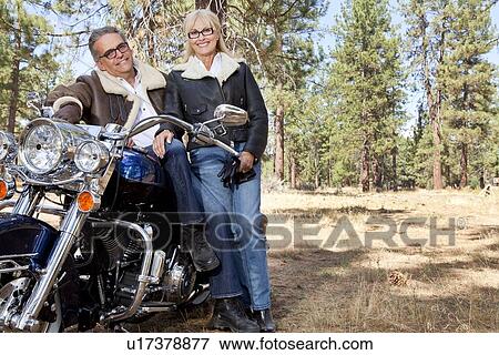 Stock Photo - Senior couple lean on motorcycle in forest. Fotosearch