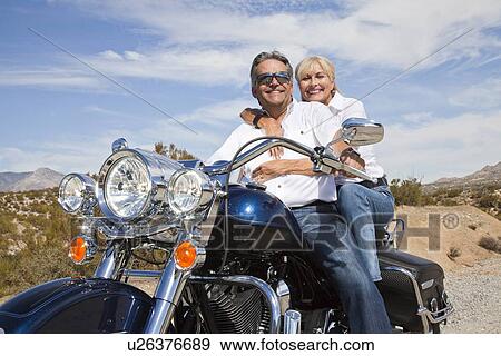 Senior couple on desert road sitting on motorcycle looking at camera View Large Photo Image Stock Photo - Senior couple on desert road sitting on motorcycle looking at camera. Fotosearch