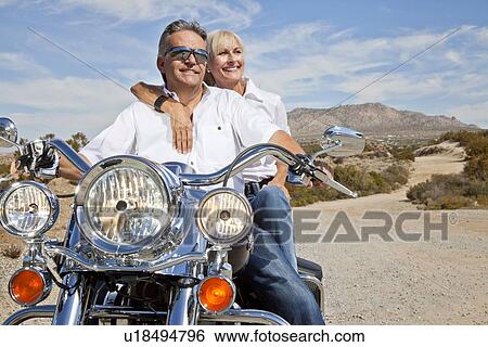 Stock Photograph - Senior couple on desert road sitting on motorcycle. Fotosearch