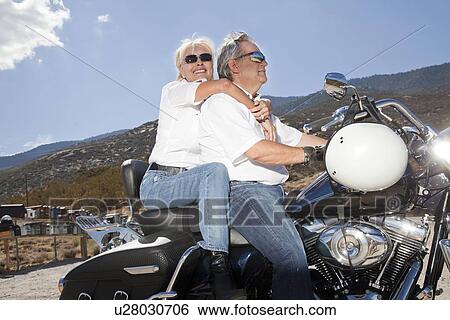 Stock Photograph - Senior couple riding a motorcycle together in a rural landscape. Fotosearch