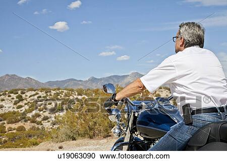 Stock Image - Senior man riding motorcycle through the desert. Fotosearch