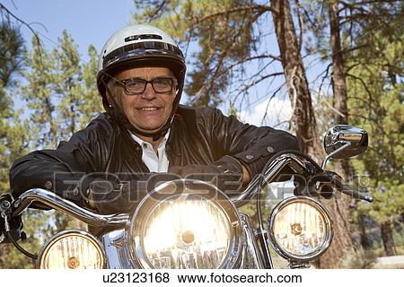 Senior man wearing helmet leaning on motorcycle handlebars in forest View Large Photo Image Stock Photo - Senior man wearing helmet leaning on motorcycle handlebars in forest. Fotosearch