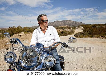 Stock Photo - Senior man wearing sunglasses on motorcycle in desert. Fotosearch