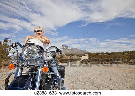Senior woman in sunglasses poses on motorcycle on desert road View Large Photo Image Stock Image - Senior woman in sunglasses poses on motorcycle on desert road. Fotosearch