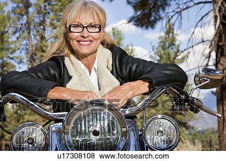 Stock Photo - Senior woman leaning on motorbike handlebars. Fotosearch