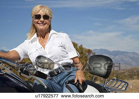 Stock Photo - Senior woman sitting on motorcycle on desert road. Fotosearch