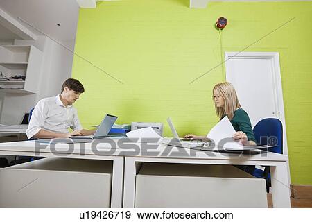 Stock Photo - Side view of young businesspeople busy working in office. Fotosearch