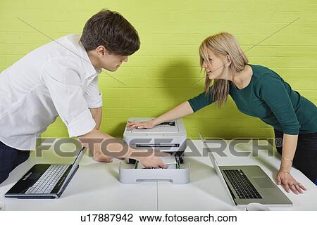 Side view of young businesspeople setting up printer with laptops at desk View Large Photo Image Stock Image - Side view of young businesspeople setting up printer with laptops at desk. Fotosearch