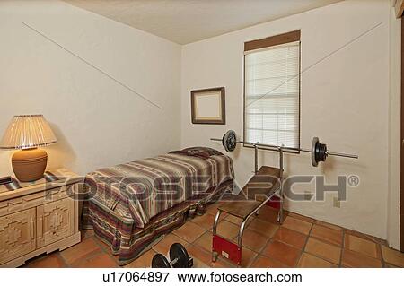 Stock Photo - Small single bedroom with bench press and weights. Fotosearch