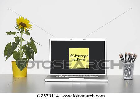 Picture - Sunflower plant on desk and sticky notepaper with Dutch text on laptop screen saying "Tijd doorbrengen met Familie" (Spending time with family). Fotosearch