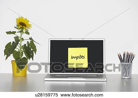 Stock Photography - Sunflower plant on desk and sticky notepaper with French text on laptop screen saying "impôts" (taxes). Fotosearch